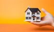 House model in woman hand on orange background. Real estate concept.