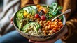 A woman holding a bowl filled with a nutritious combination of quinoa, avocado, chickpeas, and assorted vegetables, promoting a healthy and balanced meal.