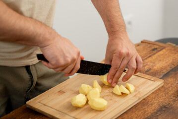 Wall Mural - Cook slicing peeled potatoes for dinner preparation on a wooden board.