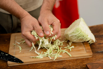 Wall Mural - Making fresh coleslaw: hands shredding cabbage on wooden board.