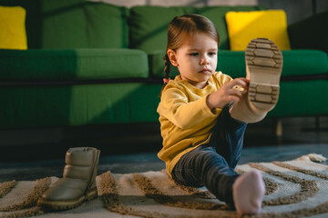 girl toddler child puts on her own boots in the winter at home