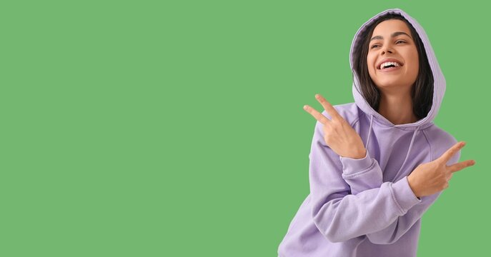 Young woman showing victory gesture on green background with space for text