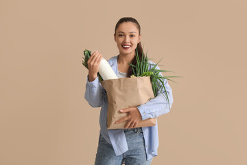 Sticker - Young Asian woman with milk bottle and shopping bag full of fresh food on brown background