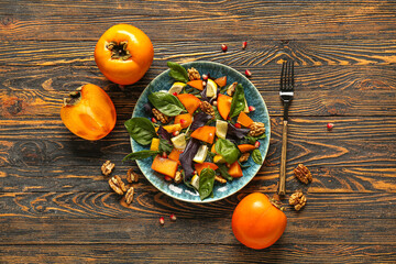 Plate of delicious salad with persimmon, walnut and pomegranate seeds on wooden background