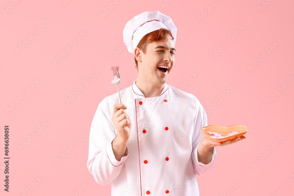 Male chef holding plate with paper hearts and fork on pink background. Valentine's Day celebration