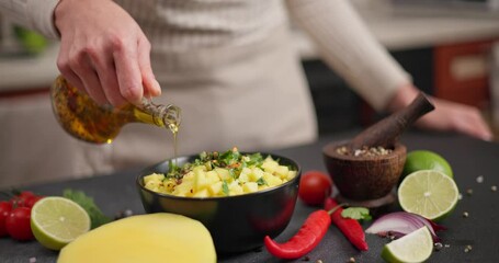 Canvas Print - Woman pouring olive oil onto Chopped sliced mango in black ceramic bowl at domestic kitchen