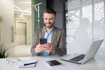 joyful smiling satisfied businessman typing text message on phone, man in business suit browsing soc