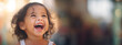 Joyful little girl with open mouth, curly hair and shining eyes laughing on bright abstract background in sunlight. Childish carefree. Close-up portrait child. Ultra wide banner. Copy space