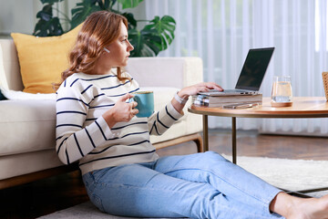 Wall Mural - Young woman using laptop while sitting behind table at home