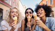 © Malynka - Three cheerful teenage women eating ice cream cones on city street , Happy female tourists enjoying summer vacation, Laughing girl friends taking selfie picture outside , Summertime holidays