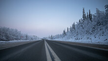 A Desolate Highway Stretches Through A Snowy Forest Landscape, Evoking Concepts Of Winter Travel And Remote Destinations