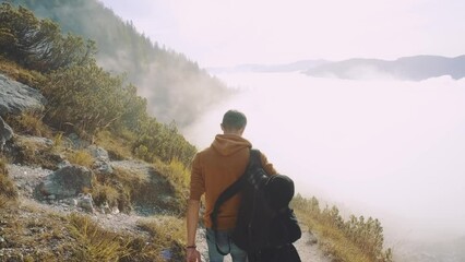 Wall Mural - Man traveler walks through the forest higher than clouds to the mountains. Incredibly beautiful views in the Alpine mountains. Hiking route in the Alps mountains in autumn. Slow motion