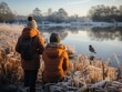 Two people birdwatching in winter gear observe a bird by a frosty lakeside at sunrise, their warm jackets contrasting with the cold blue of the frost-covered reeds.