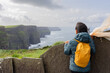 Woman on her back with backpack enjoying a splendid view from the top of the Mother's cliff in Ireland