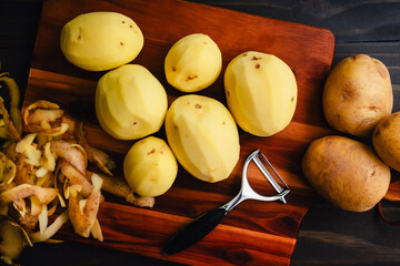 Wall Mural - Peeled Yukon Gold Potatoes on a Wooden Cutting Board: Peeled and unpeeled golden yellow potatoes with a vegetable peeler on a wood table