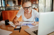 © Geber86 - Focused young woman reviewing documents while working on her laptop at home