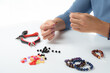 Jewelry making. Making a bracelet of colorful beads. Female hands with a tool on a white background. Selective focus.