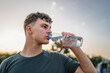 © Miljan Živković - caucasian man teenager open plastic bottle of water outdoor in sunny day drink while hold basketball