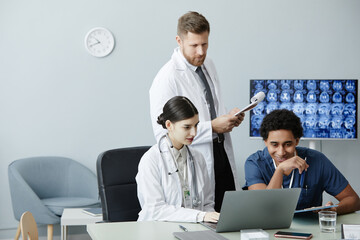 Wall Mural - Multiethnic group of doctors using laptop and looking at X-ray images together in clinic, copy space