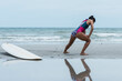 © Anatta_Tan - Asian woman standing on the beach, she is warming up by stretching her leg. before surfing in the sea. to people recreation and exercise by surf concept.