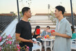 © Prathankarnpap - Two young handsome men having drinks and chatting at the rooftop party in the evening.