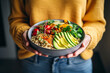© Oscar - Image created with AI. Healthy vegetarian dinner. Woman in jeans and warm sweater holding bowl with fresh salad, avocado, grains, beans, roasted vegetables, close-up. Superfood, clean eating, vegan, d