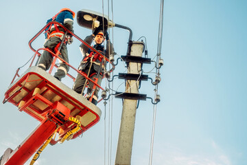 Two electricians from cradle of aerial platform or crane are repairing street lighting lamp. Professional electricians wearing helmets, overalls and insurance work at heights. View of workers from