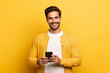 © Uzair - man looking at phone standing isolated on yellow background