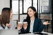 © NINENII - female colleague of half Asian descent holds a cup of coffee and smiles happily.