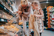 © Maskot - Senior woman buying bread with granddaughter holding bags at grocery store
