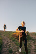 © Maskot - Smiling woman running down from hill against sky