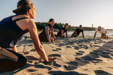 Smiling Female Instructor Doing Stretching With Team On Sand At Beach