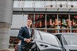 © Maskot - Businessman disembarking from car in front of building
