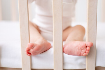 legs baby 6 months old boy on a white bed in a bright bedroom in a cotton bodysuit, the concept of children's goods