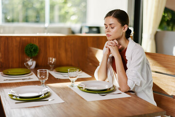 Stylish woman sitting at dining table drinking water from a glass, home modern interior, sunset light, lifestyle in comfort.