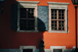 A young girl in a green down jacket and angora hat stands in profile near a terracotta-colored wall with windows and shutters in the rays of the setting sun with a dark shadow.Lviv, Armenian courtyard