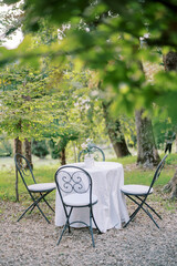 Wall Mural - Table with a white tablecloth and a bouquet of flowers stands surrounded by chairs in the park