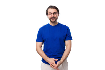 Wall Mural - young confident brunette man with a beard dressed in a blue t-shirt on a studio white background