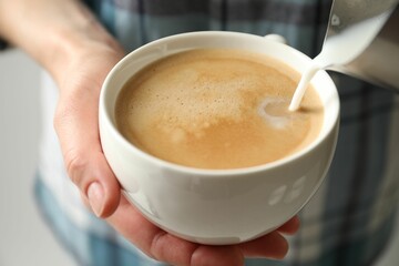 Wall Mural - Woman pouring milk into cup of hot coffee, closeup