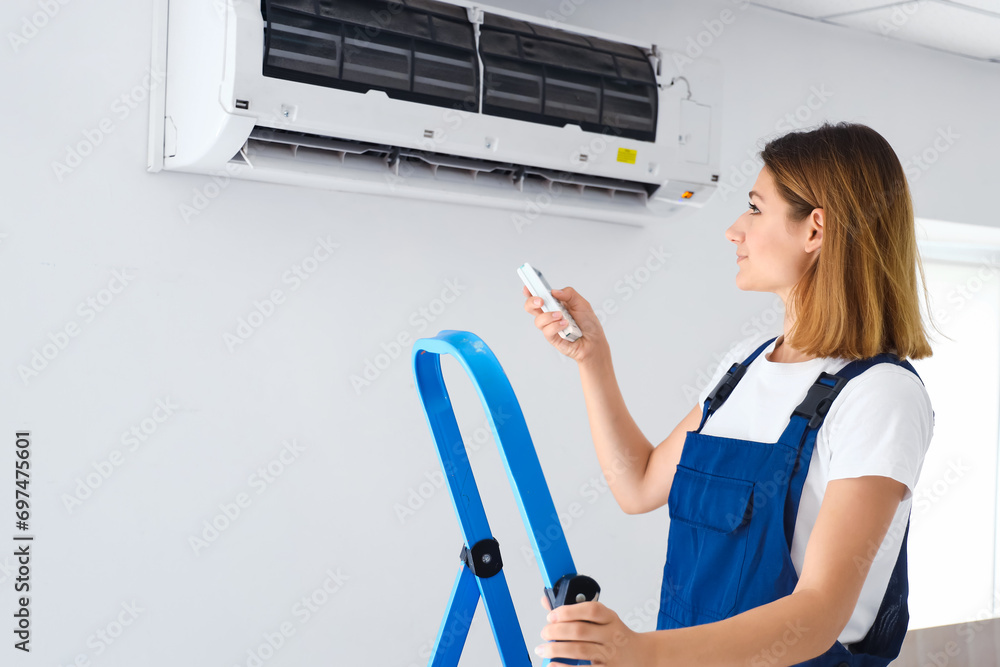 Female technician switching on air conditioner in room