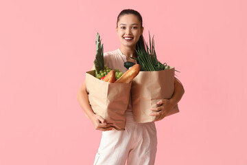 Poster - Young Asian woman with shopping bags full of fresh food on pink background