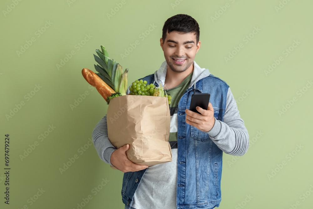 Young man with grocery bag using mobile phone on green background