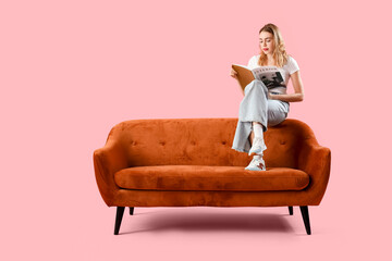 Canvas Print - Young woman reading magazine on sofa against pink background