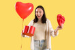 Young woman with heart-shaped balloon and open gift box on yellow background. Valentine's Day celebration
