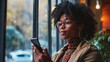 © Fotograf - A woman is seen looking at her cell phone in front of a window. This versatile image can be used to depict modern communication, technology, social media, or daily life activities