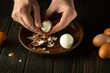 A cook peels a boiled egg from its shell on the kitchen table with his hands. Healthy eggs white diet concept. Advertising space.