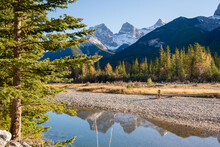 Beautiful Bow River Scenery. Canmore, Alberta, Canada. The Three Sisters Trio Of Peaks Over The Blue Sky In The Background.