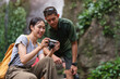 © wattana - Happy young couple sitting at tropical waterfalls and checking pictures on camera. Vacation and traveling lifestyle concept.