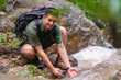 © wattana - Handsome male traveller with backpack touching cold clean mountain stream.