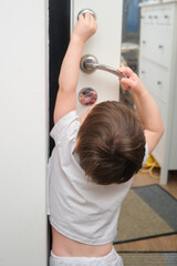 Wall Mural - Toddler baby opens the door of the house. A child in a white T-shirt. Kid aged two (two year old)